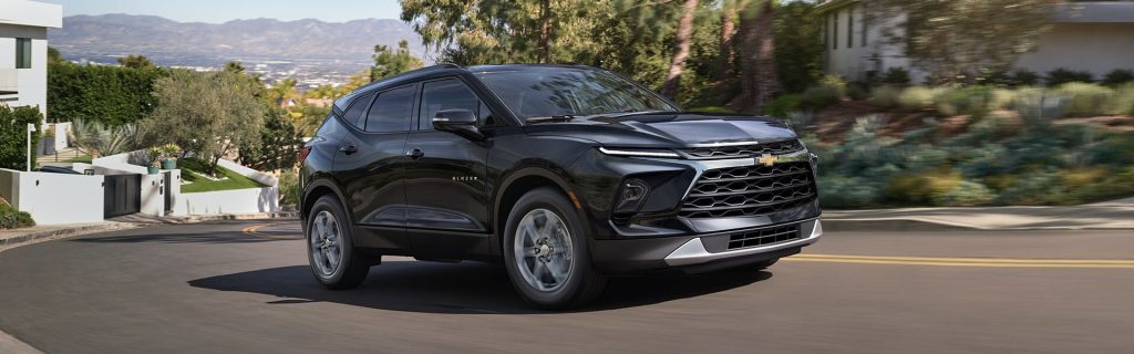 2025 Chevrolet Blazer in black driving through a modern neighborhood, highlighting its sleek exterior design and confident road presence.