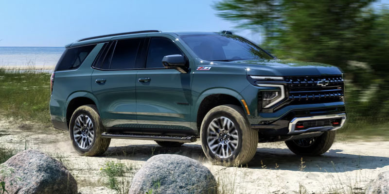 Exterior of a green 2025 Chevrolet Tahoe SUV driving on sand near a beach in North Carolina.