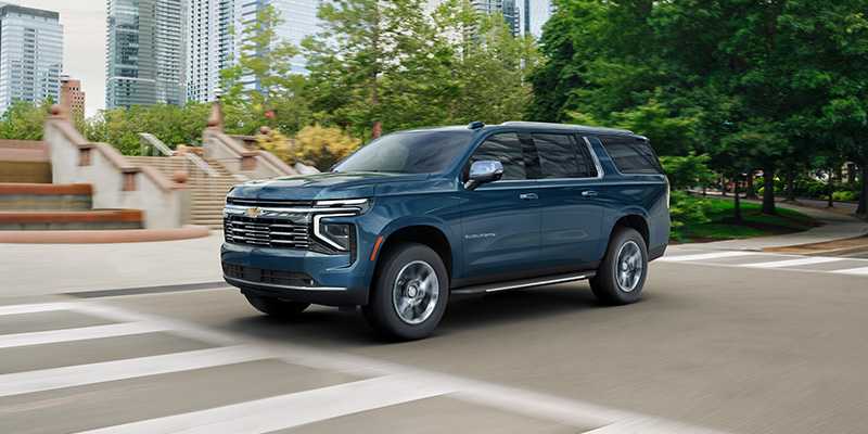 A blue Chevrolet Suburban SUV driving down a city street.