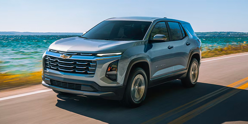 Silver Chevrolet Equinox SUV driving on a coastal road next to the ocean.