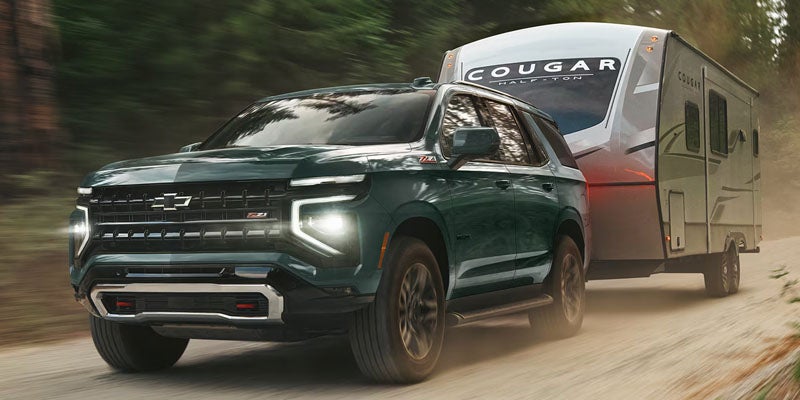 Dark green Chevrolet Tahoe towing a travel trailer along a forest road.